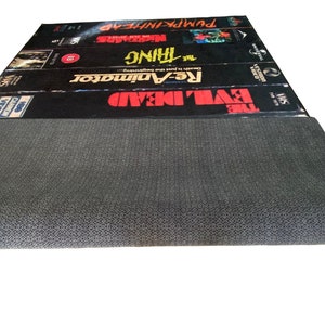 May include: A black and gray VHS tape rug with the titles "The Evil Dead", "Re-Animator", "The Thing", "Madman", and "Pumpkinhead" printed on the top.