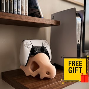 May include: A white and black game controller rests on a light peach-colored, dinosaur-shaped stand. The stand features a stylized, smooth, curved design with a small opening near the base, providing a stable cradle for the gaming peripheral.