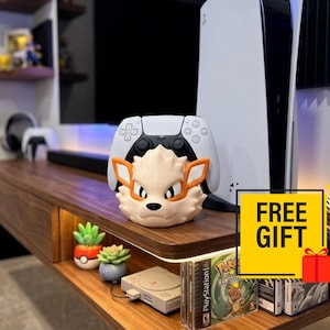 May include: A cream and orange Arcanine-themed controller stand holding a white and black wireless game controller, positioned in front of a white gaming console. A yellow square graphic with the text FREE GIFT is visible on the right side.