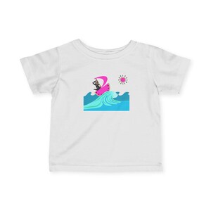 May include: A white short-sleeve t-shirt featuring a graphic print of a black cat surfing on a slice of watermelon. The design includes a bright pink sail, blue ocean waves, and a stylized sun in the upper right corner of the illustration.