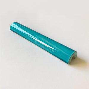 Può includere: Un pezzo di rivestimento per piastrelle in ceramica blu turchese con un bordo arrotondato e un taglio semicircolare.