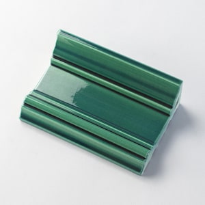 May include: A green ceramic tile with a decorative raised design. The tile has a glossy finish and is shaped like a rectangle with a curved edge.
