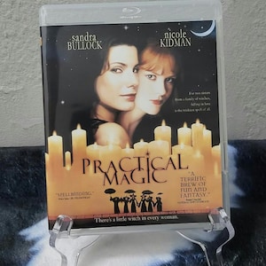 May include: A Blu-ray disc case for the film Practical Magic, featuring Sandra Bullock and Nicole Kidman on the cover. The artwork displays a dark night sky with a crescent moon, numerous lit candles, and the text Practical Magic in black.