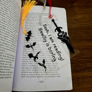 Op de afbeelding: Transparante bladwijzer met een zwart zwaard- en rozenontwerp, en de witte tekst "Seriously, I'm reading!". Met een gele kwast.