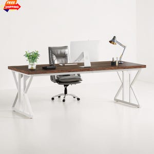 May include: A modern office desk with a dark brown wooden top and white metal legs. A silver office chair, computer monitor, desk lamp, and small plant are on the desk. The desk is in a bright, white room.