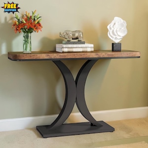 May include: A modern console table with a dark wood top and a black metal base. The table is decorated with a vase of orange flowers, a silver elephant statue, and a white floral sculpture. The table is 60 inches long.