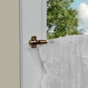 Può includere: Una tenda di pizzo bianco con un bordo smerlato è appesa a un bastone per tende color bronzo. La tenda è parzialmente tirata, rivelando la vista di un albero e un cielo nuvoloso attraverso una finestra.