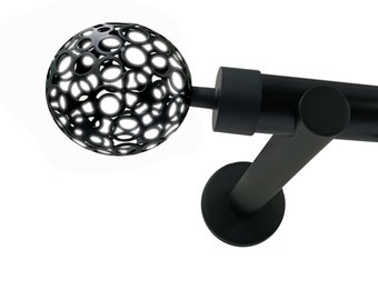 May include: Black curtain rod with a decorative orb finial featuring a cut-out pattern. The rod includes rings with clips for hanging curtains. The rod is mounted on a wall bracket.
