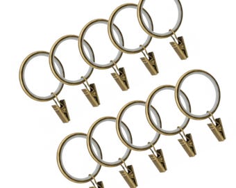 May include: A set of ten bronze-colored curtain rings with attached clips. Each ring has a circular design with a white interior and a clip for holding fabric. The clips and rings have a vintage, antique appearance.