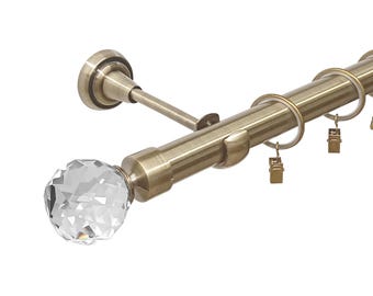 May include: A brushed brass curtain rod with crystal finials and rings. The rod is mounted to the wall with a bracket.