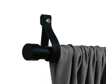 May include: Black metal curtain rod with a black leather end cap. The rod is mounted to a wall and has a gray curtain hanging from it.