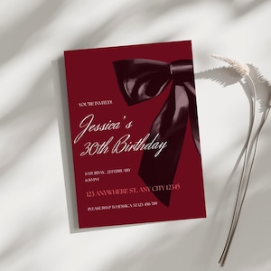 May include: A maroon invitation with a black satin bow on top. The invitation reads "You're Invited! Jessica's 30th Birthday" with the date and time of the event, the address, and RSVP information.