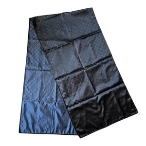 May include: A black and blue scarf with a repeating pattern. The scarf is made of a shiny material and is folded in a rectangular shape. The scarf is likely made of silk or a similar fabric.