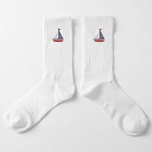 May include: Pair of white crew socks featuring a sailboat design. Each sock has a red, white, and blue sailboat embroidered near the ankle. The socks are made of a soft, comfortable material.