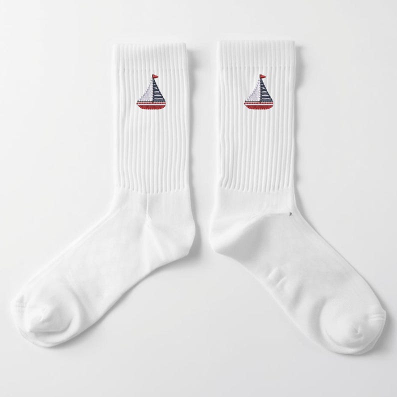 May include: Pair of white crew socks featuring a sailboat design. Each sock has a red, white, and blue sailboat embroidered near the ankle. The socks are made of a soft, comfortable material.