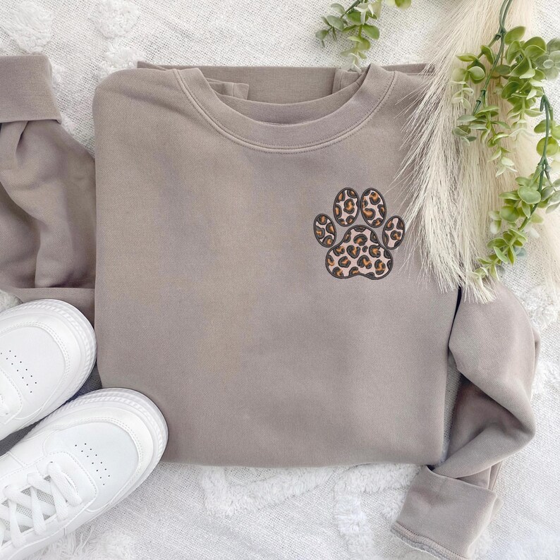 May include: A light brown sweatshirt with a leopard print paw print design on the front.