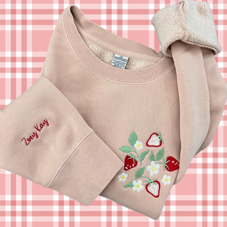 May include: A pale pink sweatshirt with a red embroidered strawberry design and the name "Zoeey Kay" embroidered on the sleeve.
