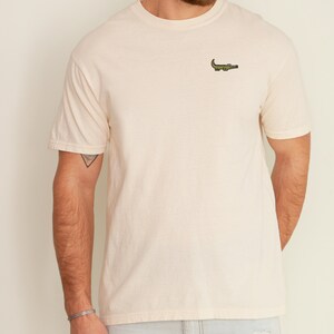 Peut inclure: Un t-shirt beige clair avec un petit alligator vert brod&eacute; sur la poitrine.