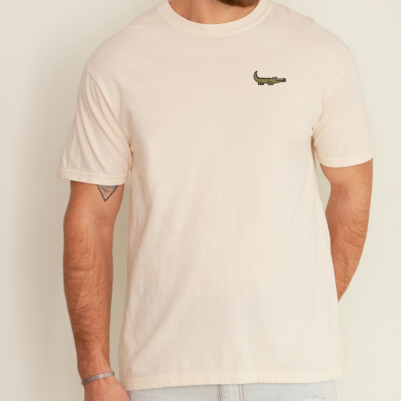 Peut inclure: Un t-shirt beige clair avec un petit alligator vert brod&eacute; sur la poitrine.