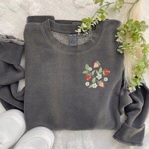 May include: A dark gray sweatshirt with a small embroidered design of strawberries and white flowers on the left chest.