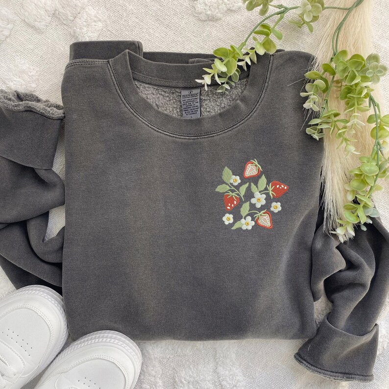May include: A dark gray sweatshirt with a small embroidered design of strawberries and white flowers on the left chest.