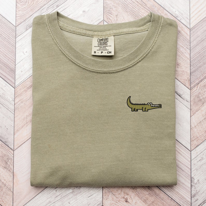Peut inclure: Un t-shirt vert pli&eacute; avec un petit alligator brod&eacute; sur la poitrine gauche. Le t-shirt porte une &eacute;tiquette indiquant "Comfort Colors" et "S - P - CH".