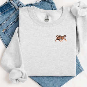 May include: A gray sweatshirt with a small embroidered tiger on the front. The tiger is orange and black with a white background.