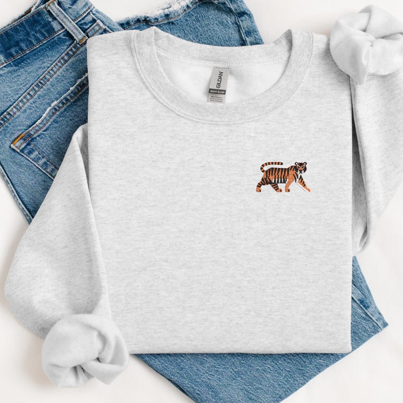 May include: A gray sweatshirt with a small embroidered tiger on the front. The tiger is orange and black with a white background.