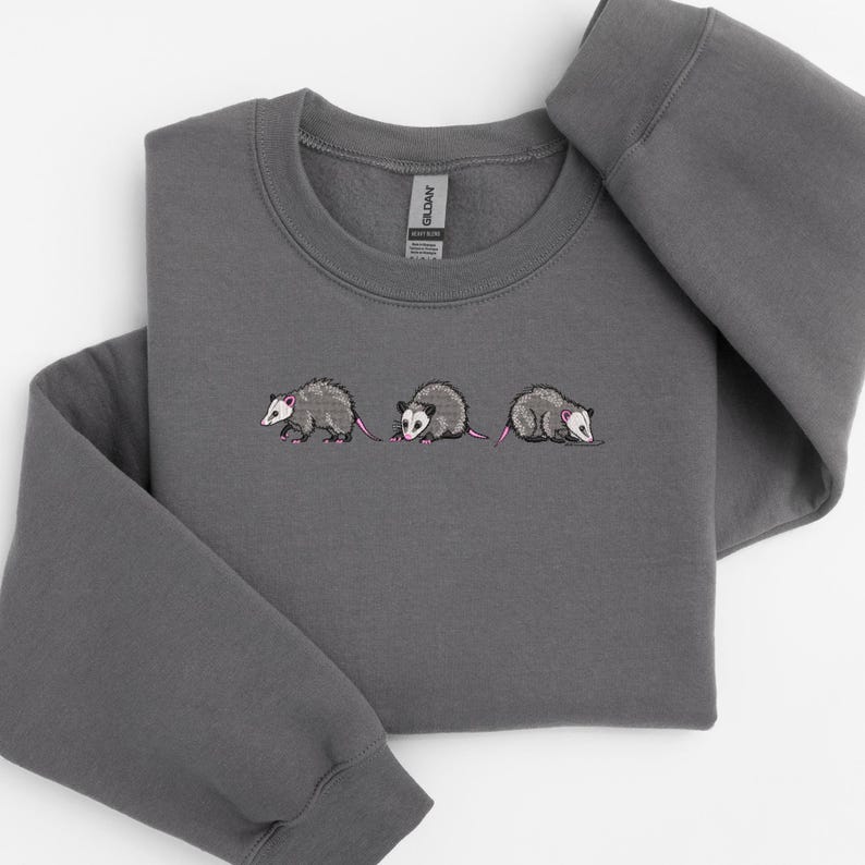 May include: A dark gray sweatshirt with an embroidered design of three opossums walking in a line. The opossums are gray with pink ears and noses.