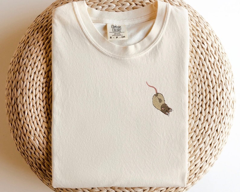 Puede incluir: Una camiseta blanca con un dise&ntilde;o de rata bordada en marr&oacute;n. La camiseta tiene cuello redondo y mangas cortas. La etiqueta de la marca dice "Comfort Colors" y "S - P - CH".