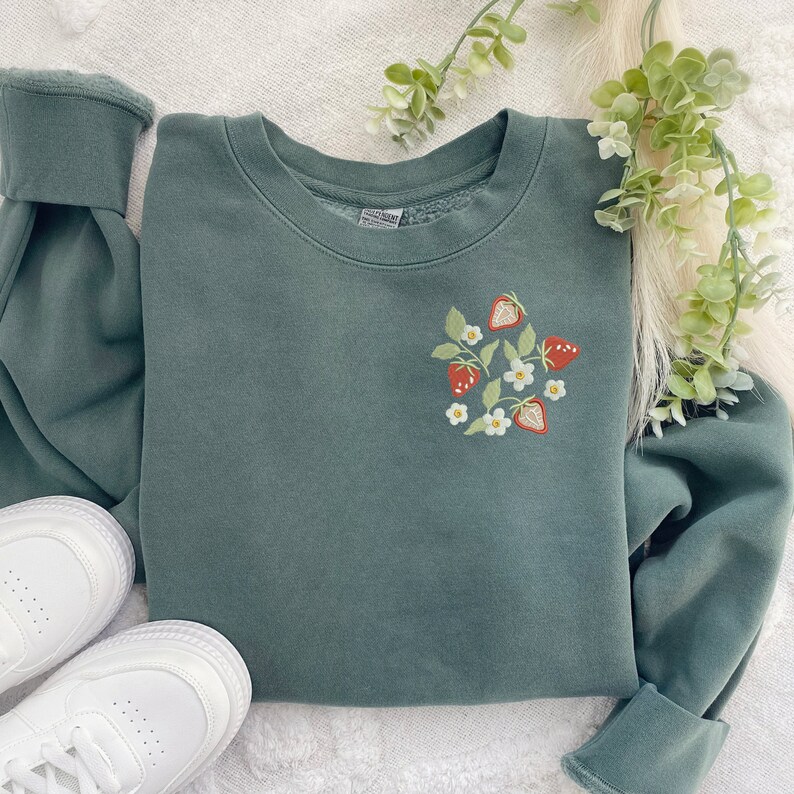 May include: A dark green sweatshirt with a white embroidered design of strawberries and flowers.