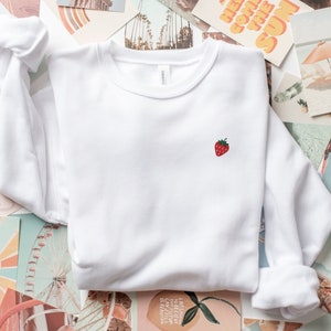May include: White sweatshirt with a small embroidered red strawberry on the left chest.