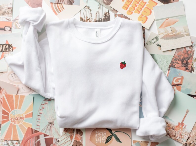May include: White sweatshirt with a small embroidered red strawberry on the left chest.