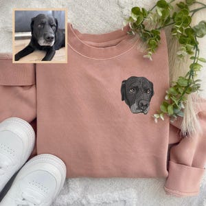 Puede incluir: Una sudadera rosa con un perro negro bordado en la parte delantera. El perro est&aacute; mirando hacia la derecha.