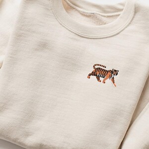 May include: A cream colored sweatshirt with an embroidered tiger design on the front.