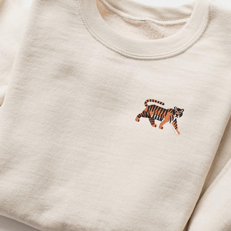 May include: A cream colored sweatshirt with an embroidered tiger design on the front.