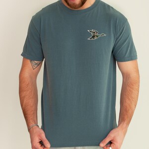 May include: A teal blue t-shirt with a camouflage duck silhouette on the front.