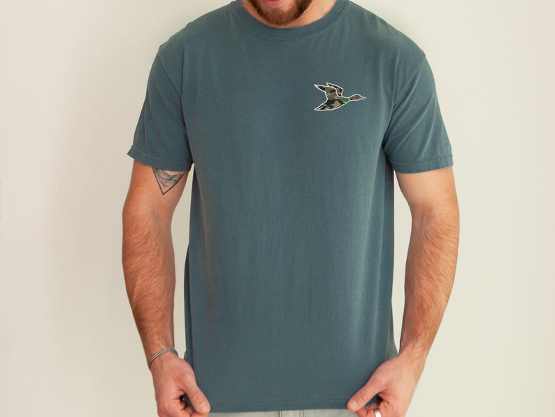 May include: A teal blue t-shirt with a camouflage duck silhouette on the front.