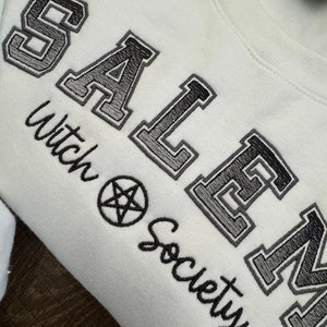 May include: White sweatshirt with black embroidered text that reads "SALEM Witch Society" with a pentagram symbol.