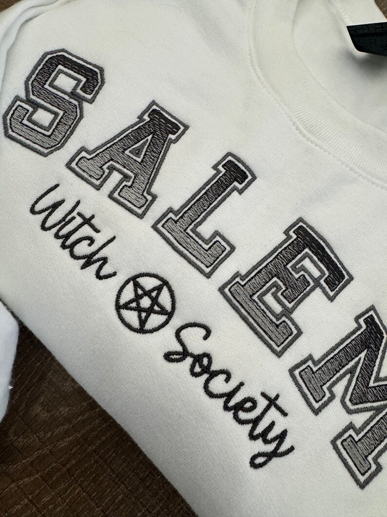 May include: White sweatshirt with black embroidered text that reads "SALEM Witch Society" with a pentagram symbol.