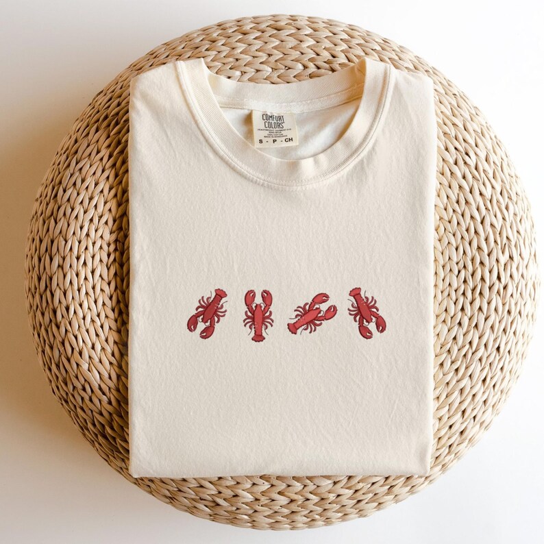 May include: A cream colored t-shirt with a red lobster design. The shirt has the text "Ocean Colors" and "S - P - CH" on the tag.