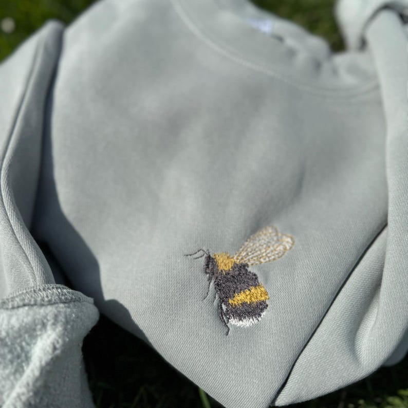 May include: A light green sweatshirt with an embroidered bumble bee design. The bee is yellow and black with brown wings.