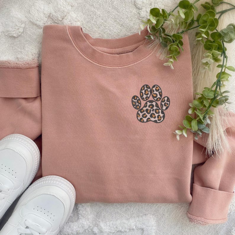 May include: A pink sweatshirt with a leopard print paw print design.