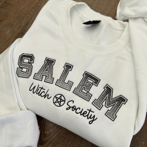 May include: White sweatshirt with black embroidered text that reads "SALEM Witch Society" with a pentagram symbol.