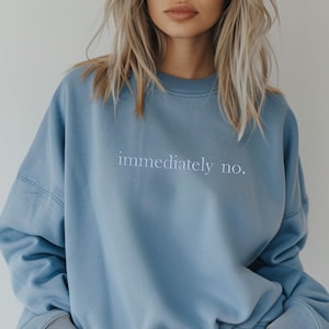 以下が含まれることがあります： 「immediately no.」と刺繍されたライトブルーのスウェットシャツ。クルーネックと長袖で、ゆったりとしたフィット感です。テキストはシンプルなサンセリフ体です。