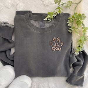 May include: A dark gray sweatshirt with a leopard print paw print design on the front.