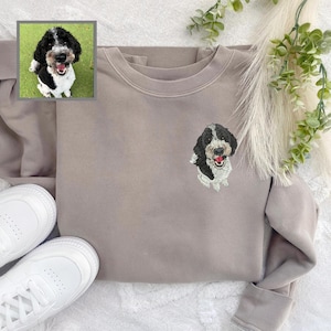 Puede incluir: Una sudadera de color marr&oacute;n claro con una imagen bordada de un perro blanco y negro en la parte delantera.