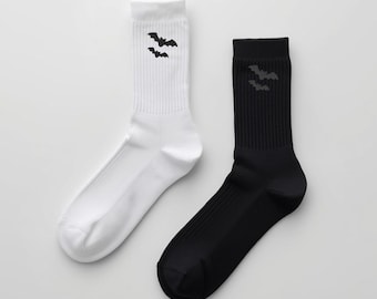May include: A pair of crew socks, one white and one black, each featuring a black bat graphic near the top. The socks are made of a ribbed knit material and are suitable for everyday wear. The bats are a Halloween theme.
