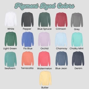 K&ouml;nnte beinhalten: Eine Auswahl an pigmentgef&auml;rbten Crewneck-Sweatshirts in verschiedenen Farben, darunter Wei&szlig;, Grau, Blau und Rosa. Jedes Sweatshirt ist mit seinem Farbnamen beschriftet, wie z. B. "Crimson" und "Butter". Der Text "Pigment Dyed Colors" befindet sich oben.