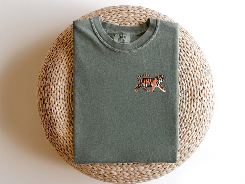 May include: A green t-shirt with an embroidered tiger design. The tiger is orange and black with a white background.